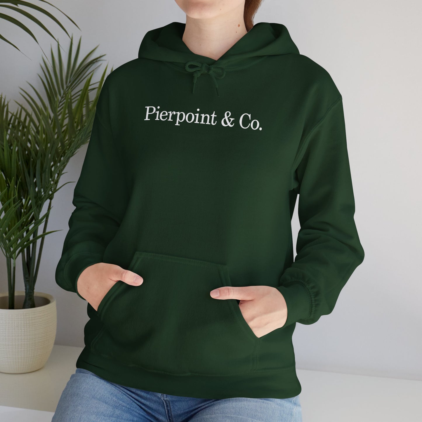 Female model wearing a green soft Unisex Hoodie Heavy Blend Hooded Sweatshirt featuring the Pierpoint & Co logo worn by the character Eric Tao in the TV show Industry.