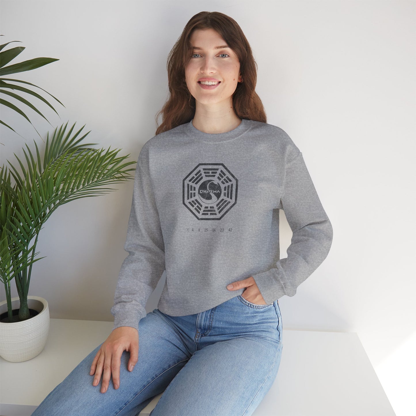 model wearing a sport heather gray Soft Gildan 18000 crew neck sweatshirt featuring the Dharma Initiative swan logo graphic from the TV show LOST in a vintage distressed ink-stamped worn-in style.