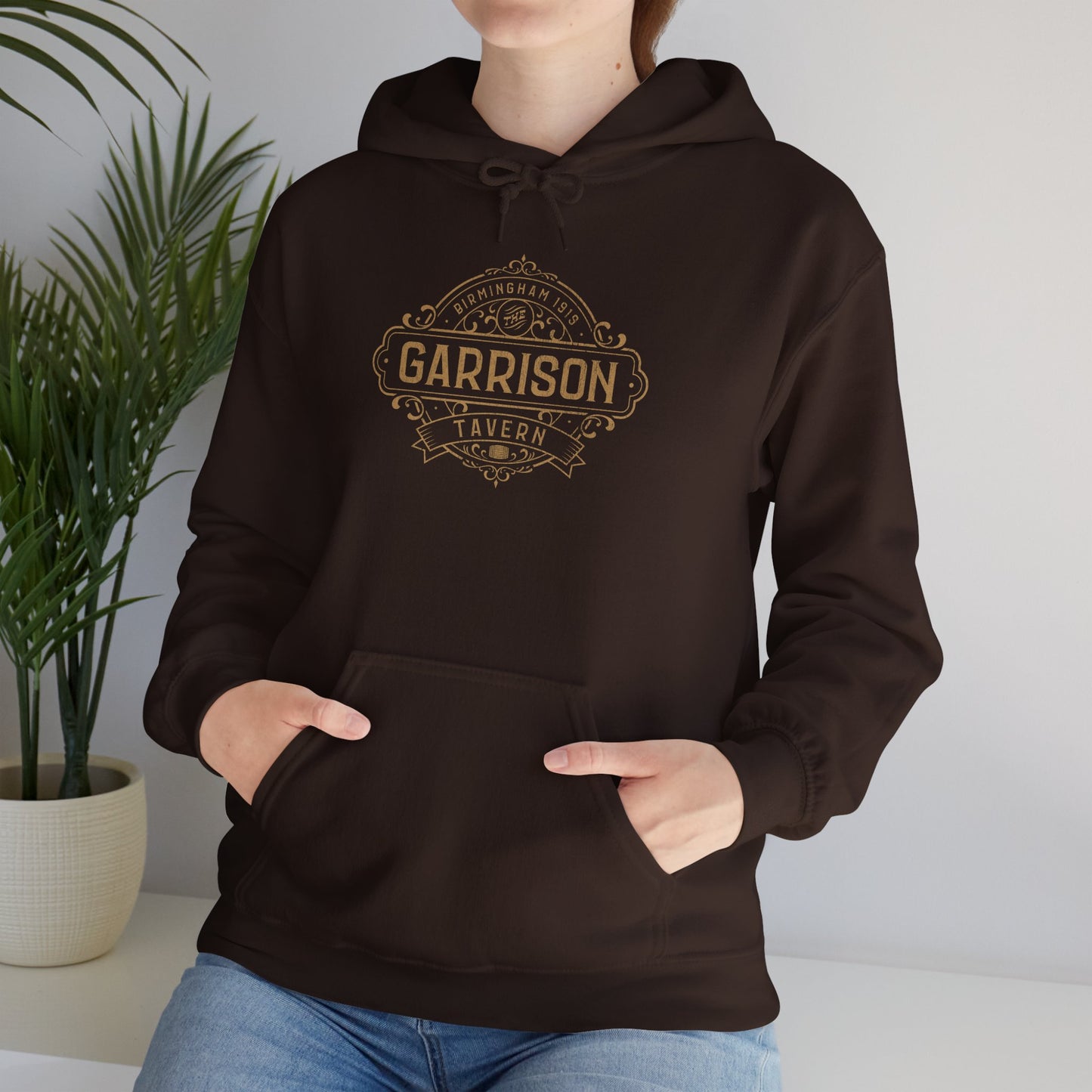 Female model wearing a dark chocolate Soft Unisex Hoodie Heavy Blend Hooded Sweatshirts featuring the Garrison Tavern Bar Logo Graphic inspired by the TV show and movie Peaky Blinders in a vintage distressed style sold by ScriptedBrand.