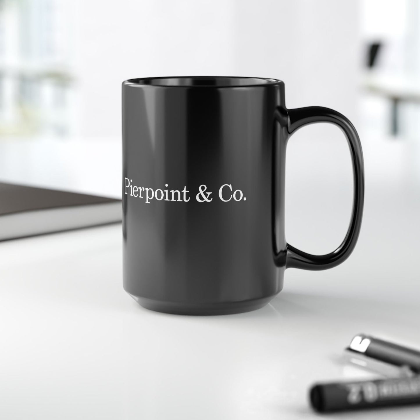 Black mug with 'Pierpoint & Co.' text on a white surface with office items.