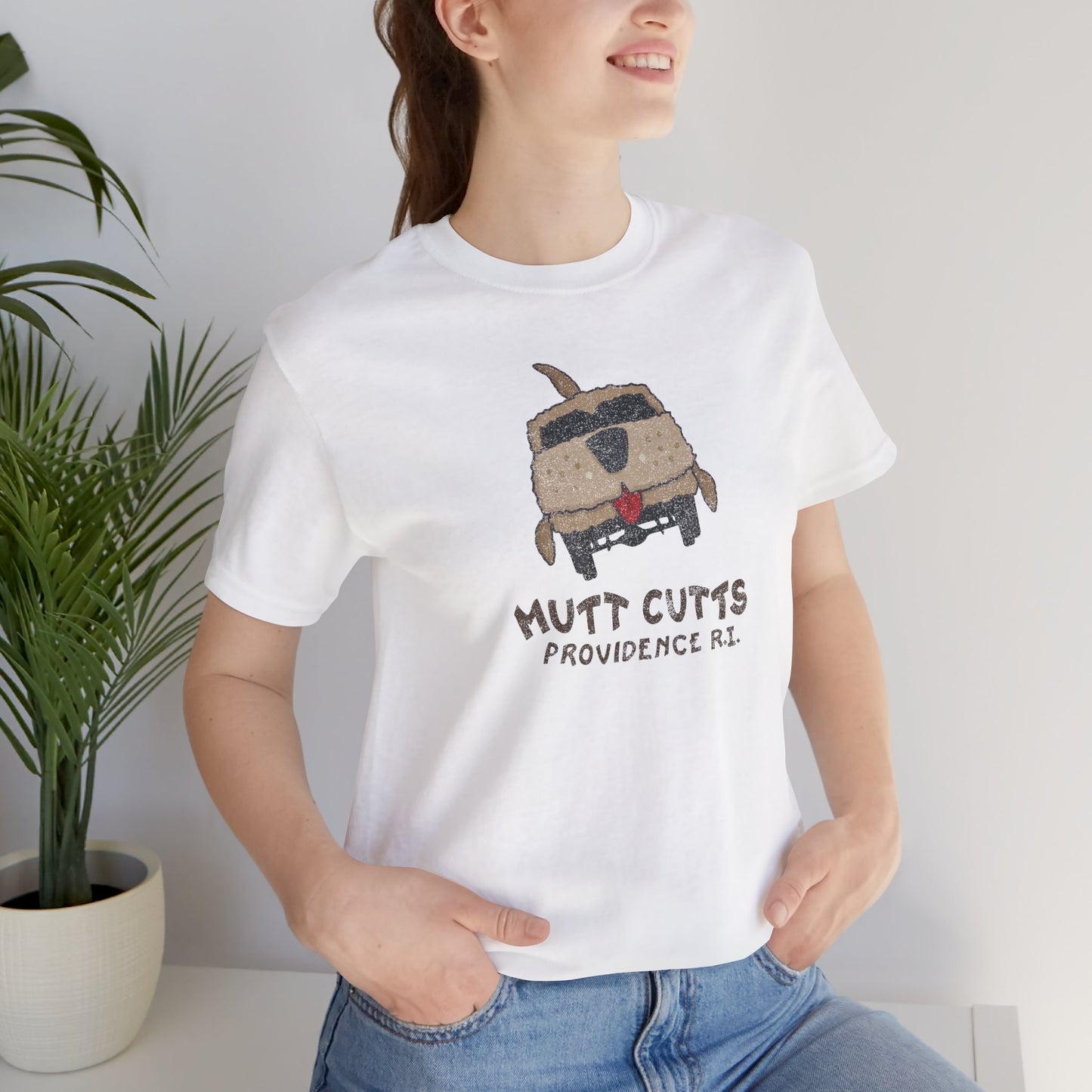 Female model wearing a white colored Soft unisex Bella+Canvas 3001 short-sleeve t-shirt featuring a Mutt Cutts logo graphic inspired by the movie Dumb and Dumber, illustrated by ScriptedBrand in a vintage distressed style.