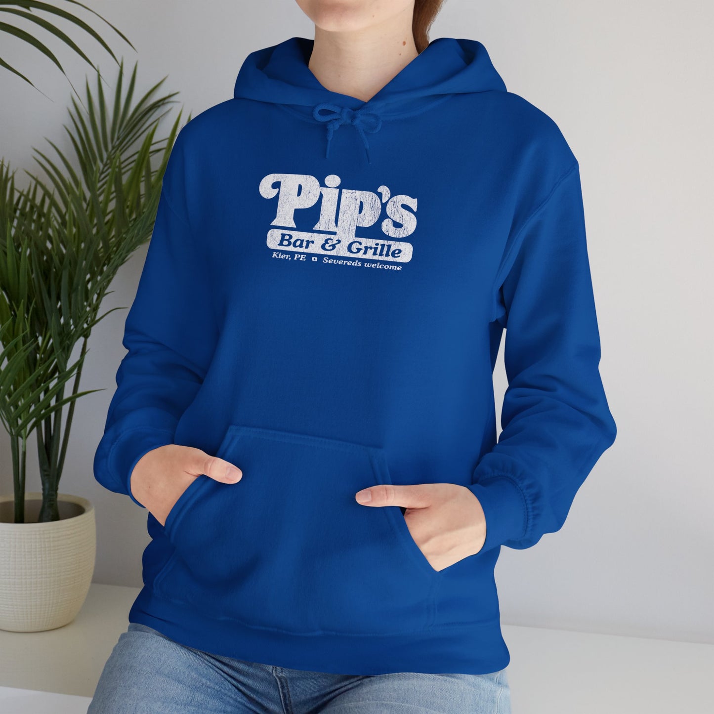 Female model wearing a royal blue colored Soft Unisex Hoodie Heavy Blend Hooded Sweatshirt featuring the Pips Bar & Grill logo, with the added text "Severeds Welcome" inspired by the TV show Severance in a vintage distressed style, sold by ScriptedBrand.