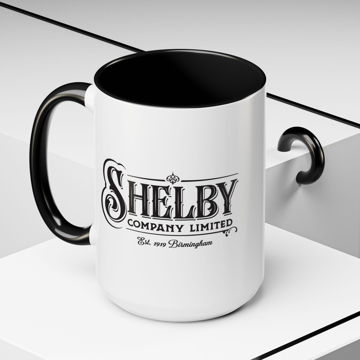Front Angled view of a 15 oz White Ceramic Mug with black handle/interior featuring the fictional Shelby Company Limited Logo from the TV show Peaky Blinders printed on both sides. Graphic is designed by ScriptedBrand and includes the text "Est. 1919 Birmingham"