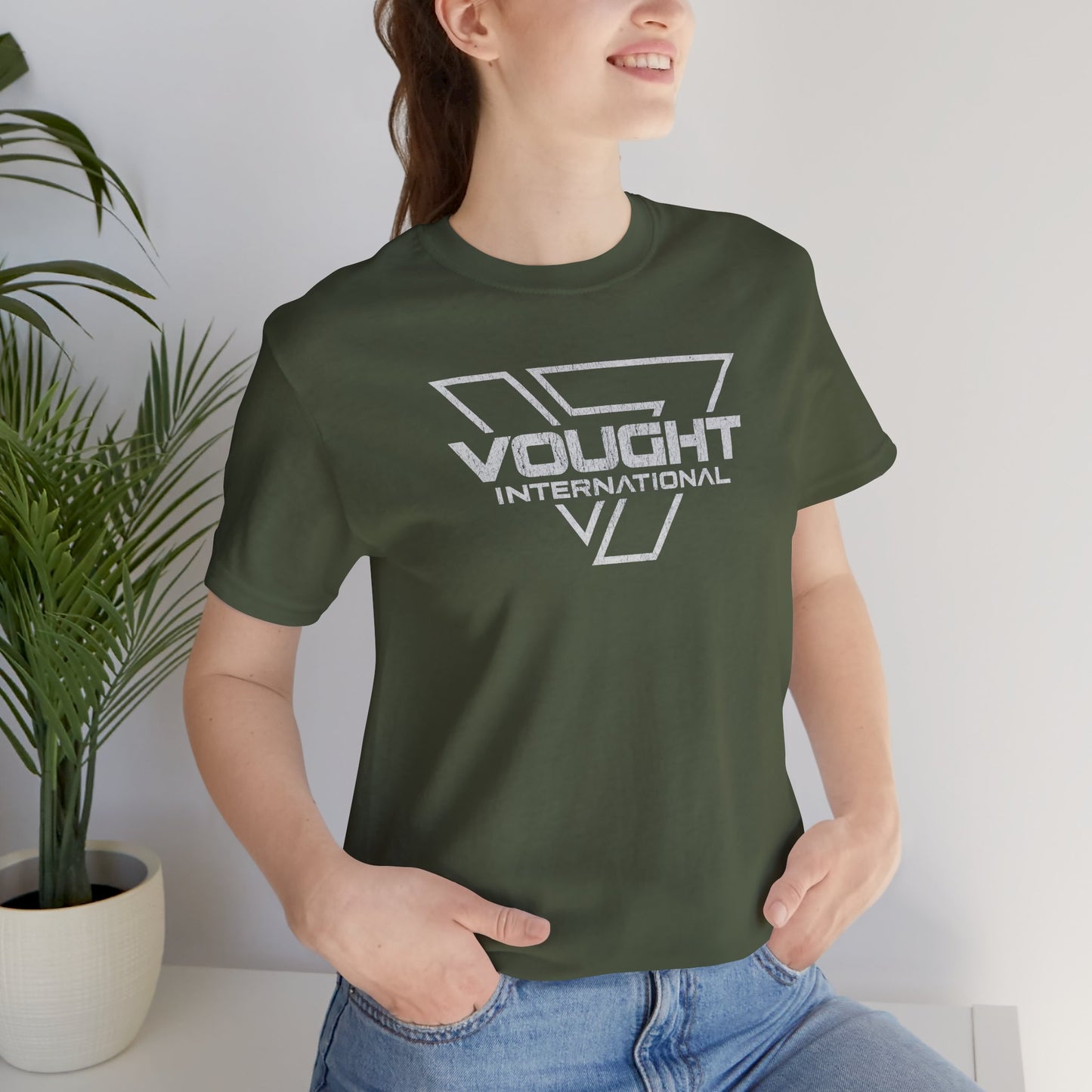 Female model wearing a military green soft Bella+Canvas 3001 short-sleeve t-shirt featuring the logo graphic of the fictional company Vought International inspired by the TV show The Boys in a vintage distressed style, sold by ScriptedBrand.