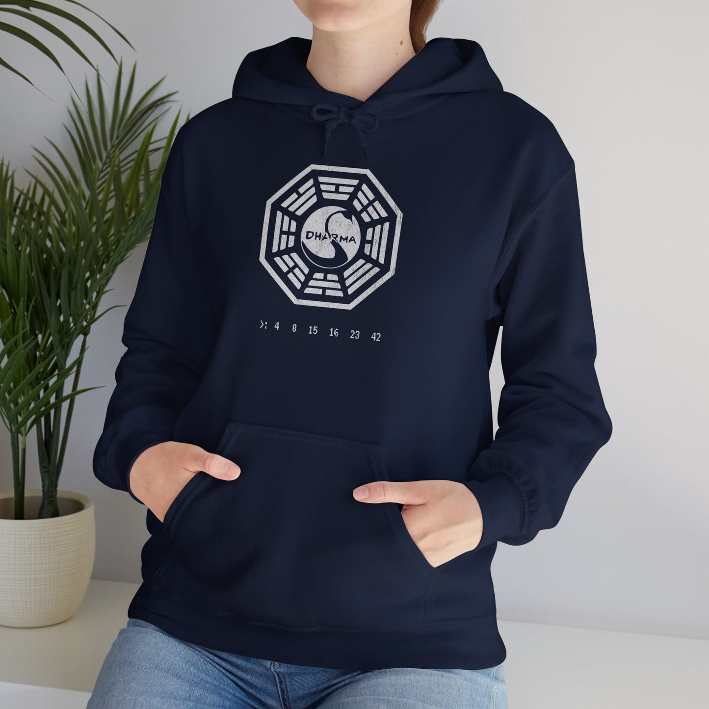 Female model wearing a navy blue Soft Unisex Hoodie Heavy Blend Hooded Sweatshirt featuring the Dharma Initiative swan logo graphic from the TV show LOST in a vintage distressed ink-stamped worn-in style.