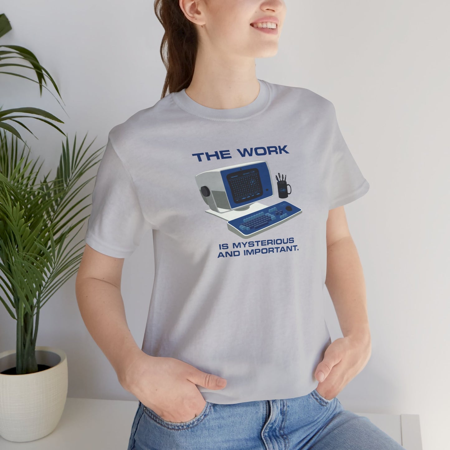 Female model wearing a solid athletic grey Soft Bella+Canvas shirtsleeve t-shirt featuring the retro computer workstation from the Apple TV show Severance, and includes the text The Work is Mysterious and Important. Graphic is designed and illustrated by ScriptedBrand.