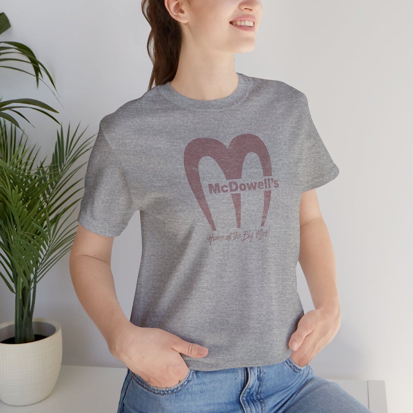Woman wearing a Heather gray t-shirt featuring the McDowells logo from the movie Coming to America in a vintage distressed style.