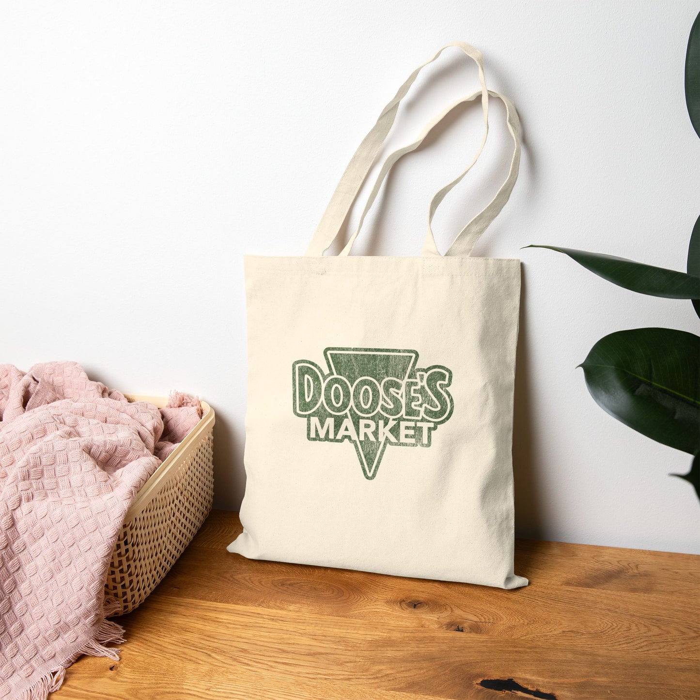Cotton canvas tote bag with vintage green Doose’s Market logo on both sides, inspired by Gilmore Girls, on a wooden surface.