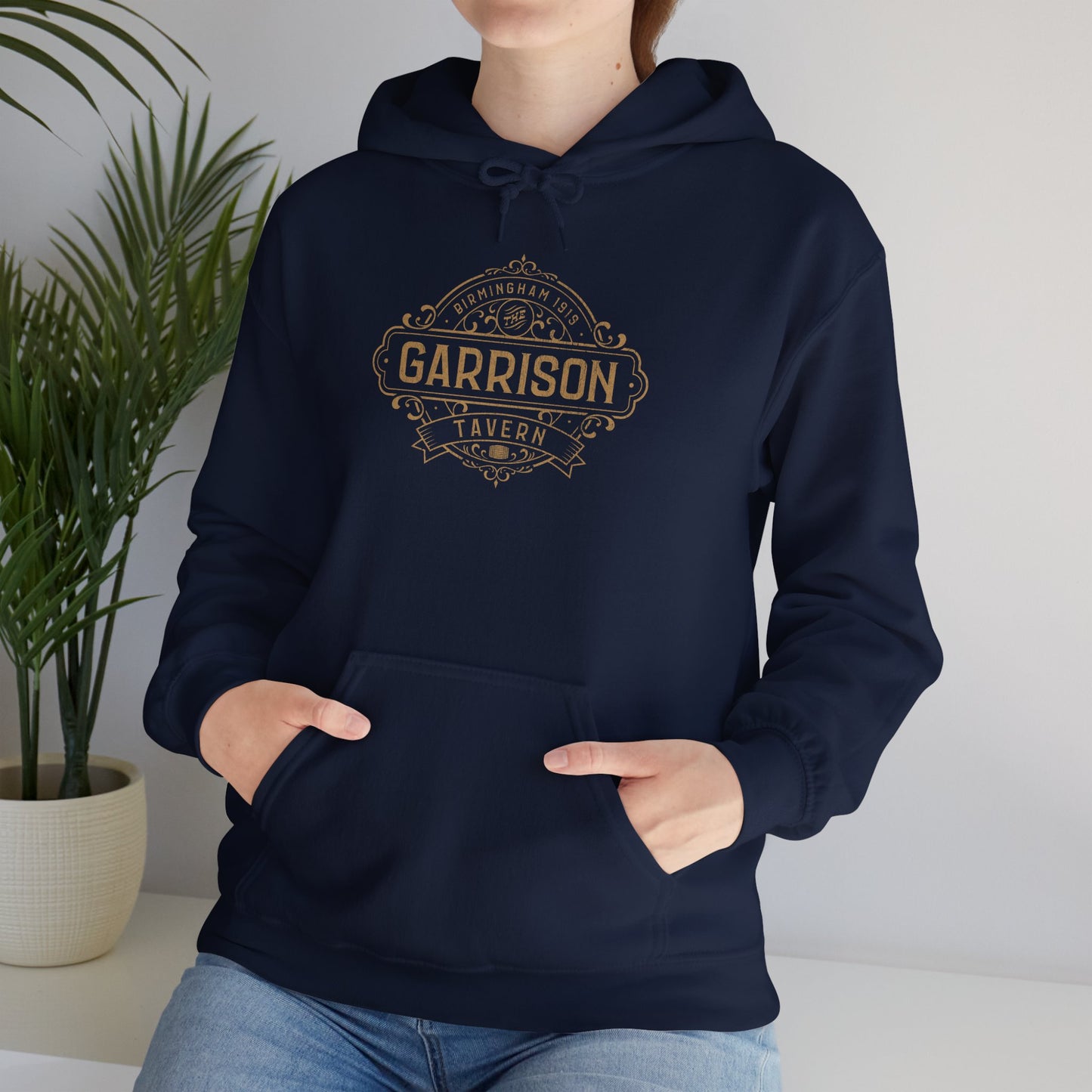Female model wearing a navy blue Soft Unisex Hoodie Heavy Blend Hooded Sweatshirts featuring the Garrison Tavern Bar Logo Graphic inspired by the TV show and movie Peaky Blinders in a vintage distressed style sold by ScriptedBrand.