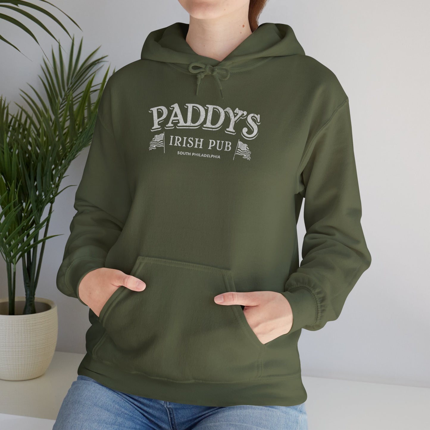 Female model wearing a military green colored soft unisex Hoodie Heavy Blend Hooded Sweatshirt featuring the Paddy's Pub logo graphic from the TV Show It's Always Sunny in Philadelphia, in a vintage distressed style, sold by ScriptedBrand.