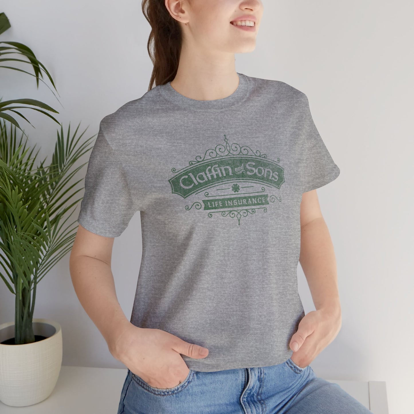 Female wearing an athletic heather grey colored soft Bella+Canvas 3001 short-sleeve t-shirt featuring a logo graphic of Claffin & Sons Insurance, designed by ScriptedBrand in a vintage distressed vintage distressed style, inspired by the TV show Bad Sisters.