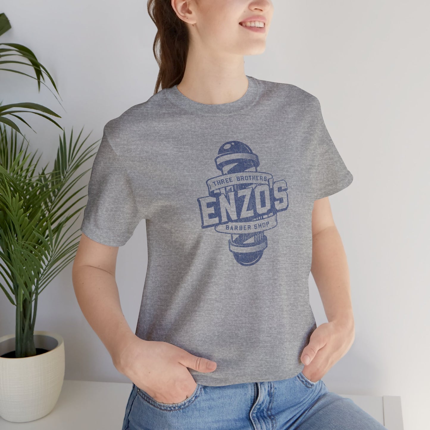 Woman wearing an athletic heather gray t-shirt with the Enzo's Barber Shop logo graphic inspired by the TV show Seinfeld in a vintage distressed style.