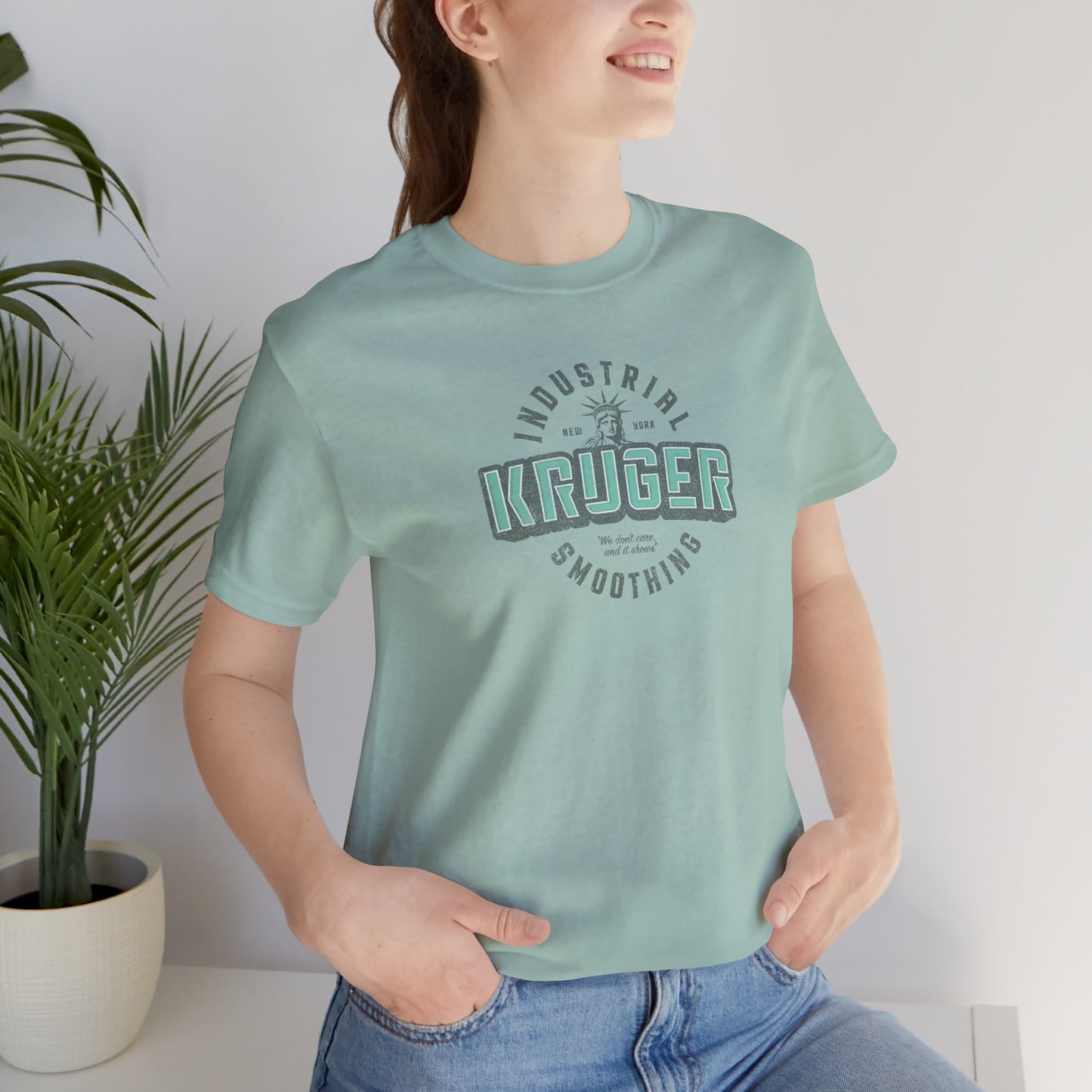 Female model wearing a dusty blue colored Soft unisex Bella+Canvas 3001 short-sleeve t-shirt featuring a Kruger Industrial Smoothing logo graphic in a vintage distressed style, designed by ScriptedBrand, and inspired by the TV show Seinfeld.