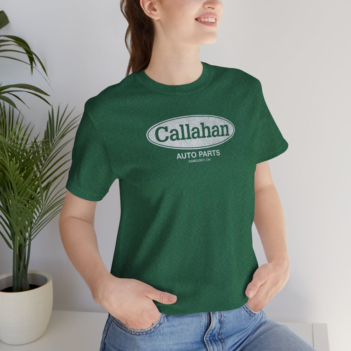 Female model wearing a Heather Grass Green colored soft short-sleeve t-shirt with the Callahan Auto Parts logo from the movie Tommy Boy in a vintage distressed style.