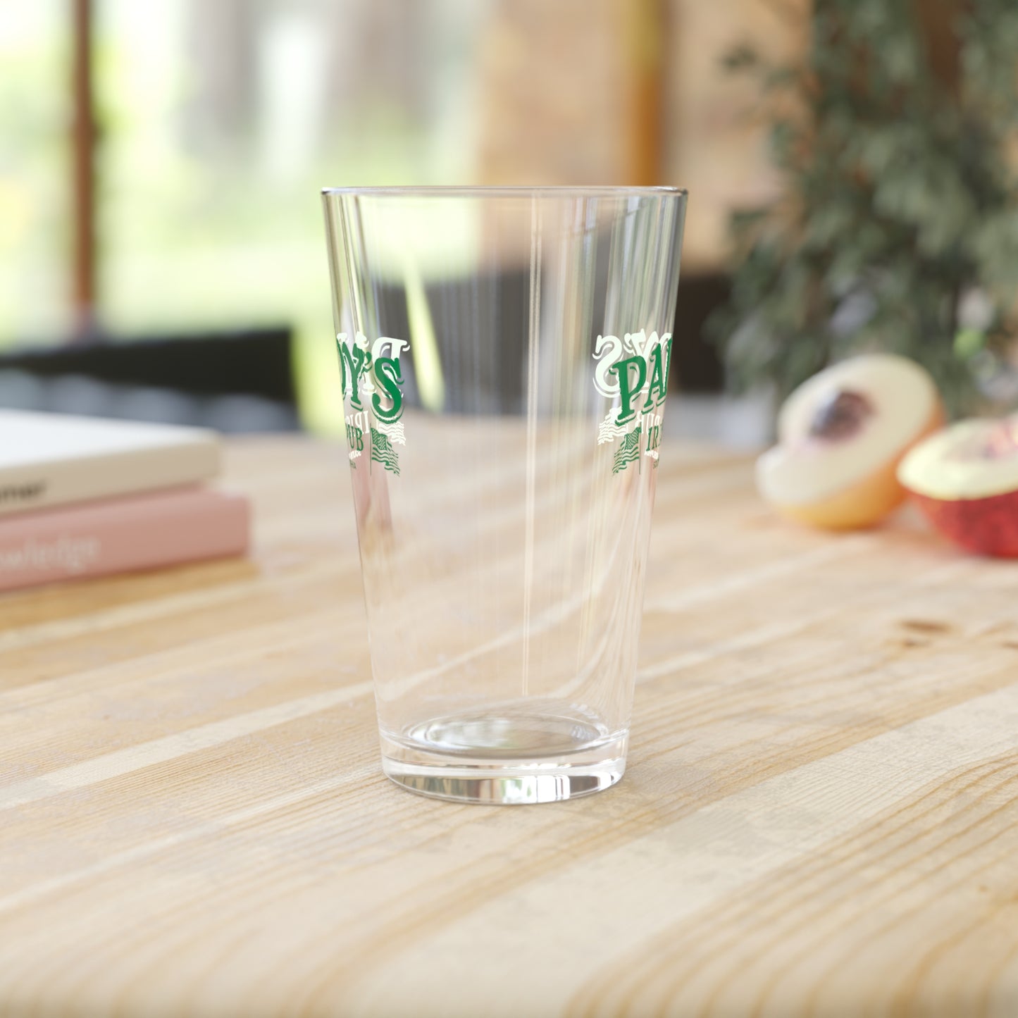 Side view of an empty 16 ounce clear pint glass featuring the Paddy's Pub logo graphic from the TV Show It's Always Sunny in Philadelphia printed on both sides, sold by ScriptedBrand.