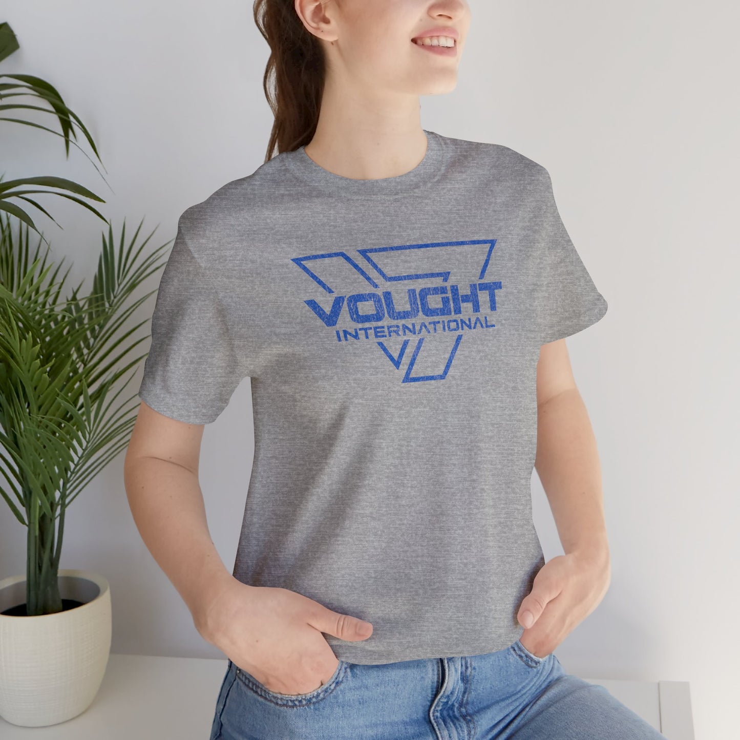 Female model wearing an athletic heather grey soft Bella+Canvas 3001 short-sleeve t-shirt featuring the logo graphic of the fictional company Vought International inspired by the TV show The Boys in a vintage distressed style, sold by ScriptedBrand.