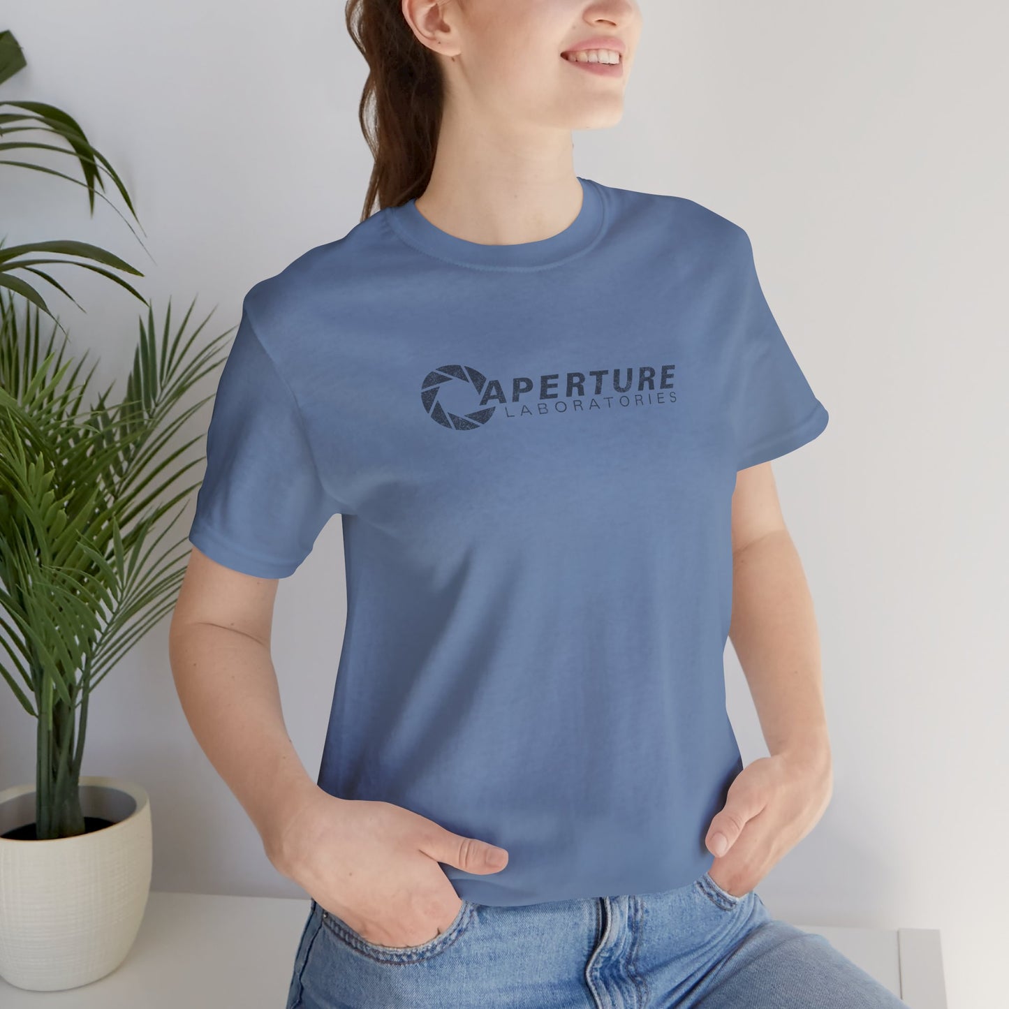 Woman model wearing a steel blue colored soft Bella+Canvas t-shirt with the Aperture Laboratories logo from the video game Portal and Portal 2 in a vintage ink-stamped distressed style.
