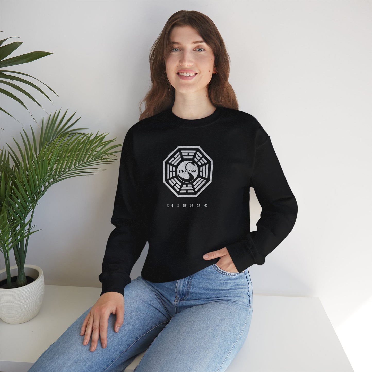 model wearing a black Soft Gildan 18000 crew neck sweatshirt featuring the Dharma Initiative swan logo graphic from the TV show LOST in a vintage distressed ink-stamped worn-in style.