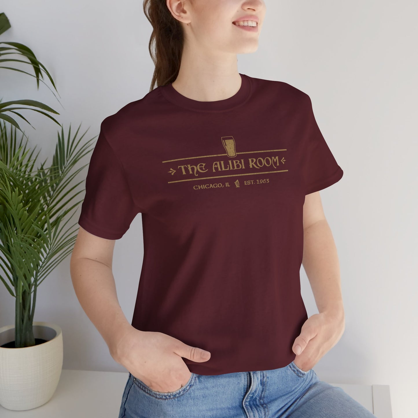 Woman wearing maroon t-shirt featuring The Alibi Room logo graphic inspired by the TV show Shameless in a vintage distressed style.