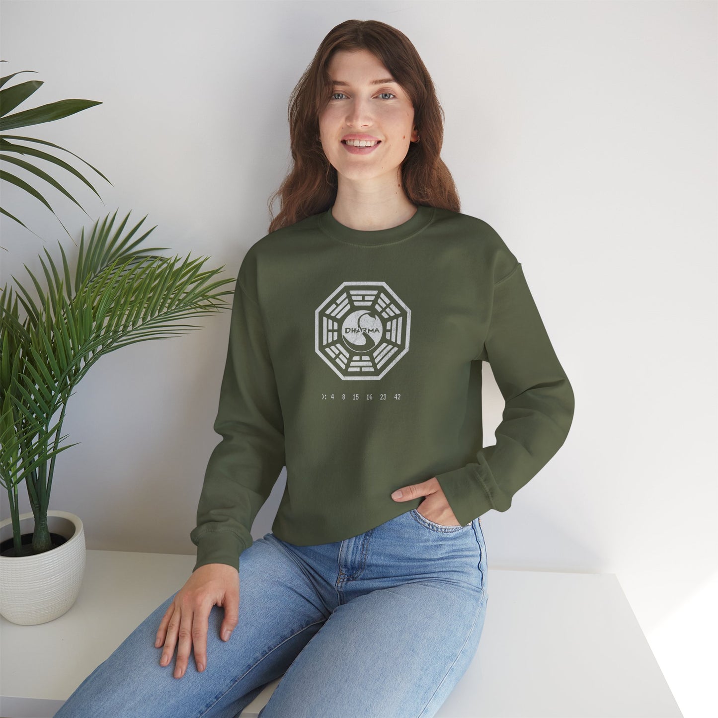 model wearing a military green Soft Gildan 18000 crew neck sweatshirt featuring the Dharma Initiative swan logo graphic from the TV show LOST in a vintage distressed ink-stamped worn-in style.