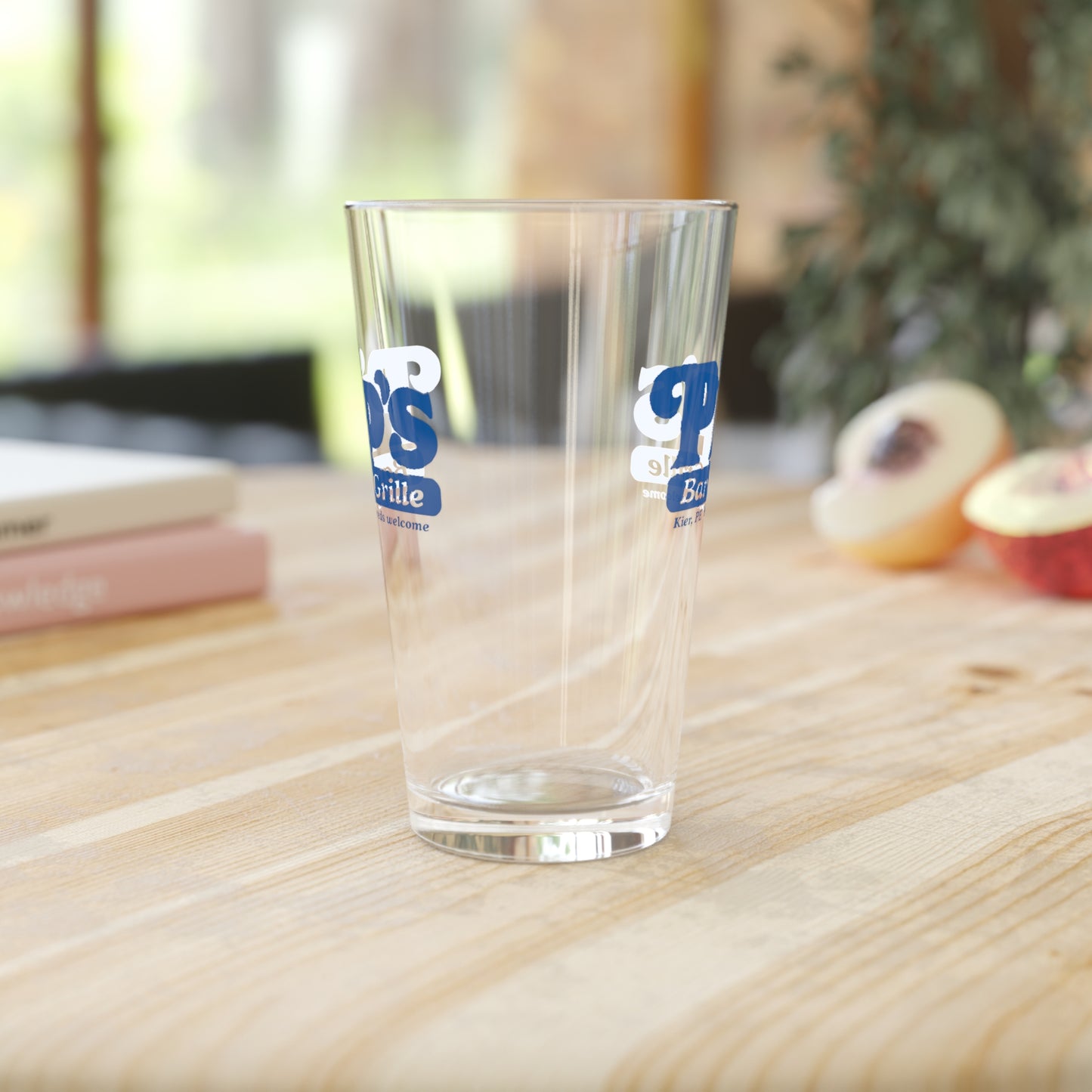 Mockup of a 16 ounce clear pint glass in a kitchen featuring the Pips Bar and Grill logo from the Apple TV show Severance printed on both sides.