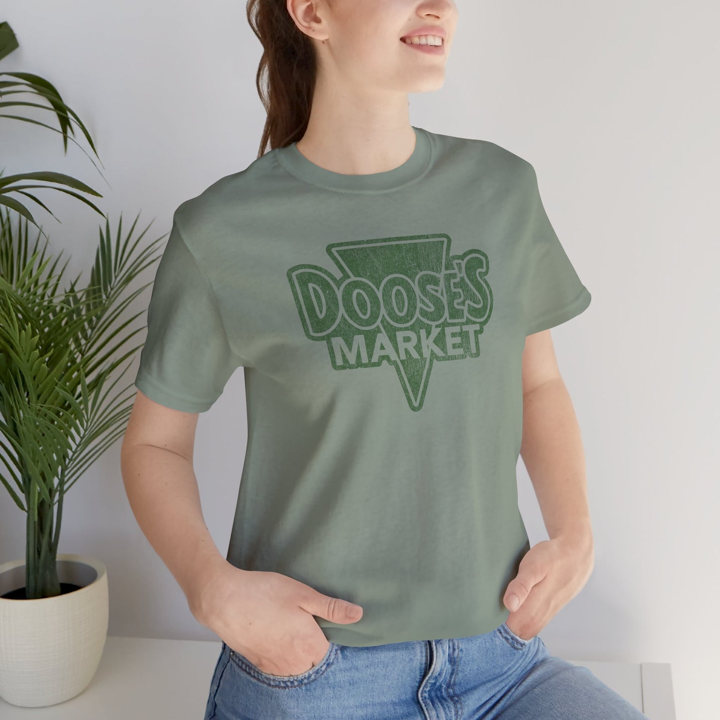 female wearing sage green Bella+Canvas t-shirt with a vintage-style Doose’s Market logo graphic, inspired by Gilmore Girls