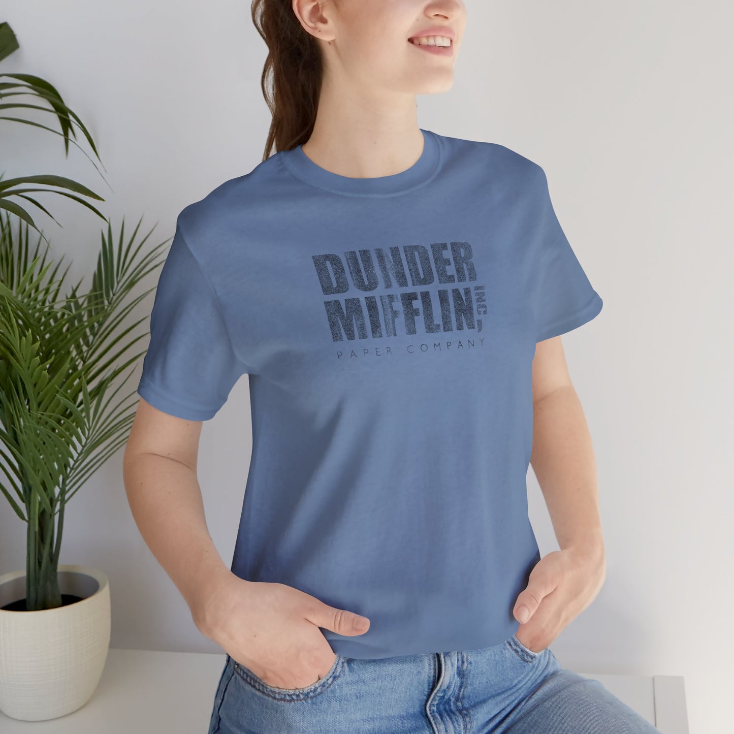 Woman wearing a steel blue t-shirt featuring the Dunder Mifflin logo from the TV show The Office in a vintage distressed style.
