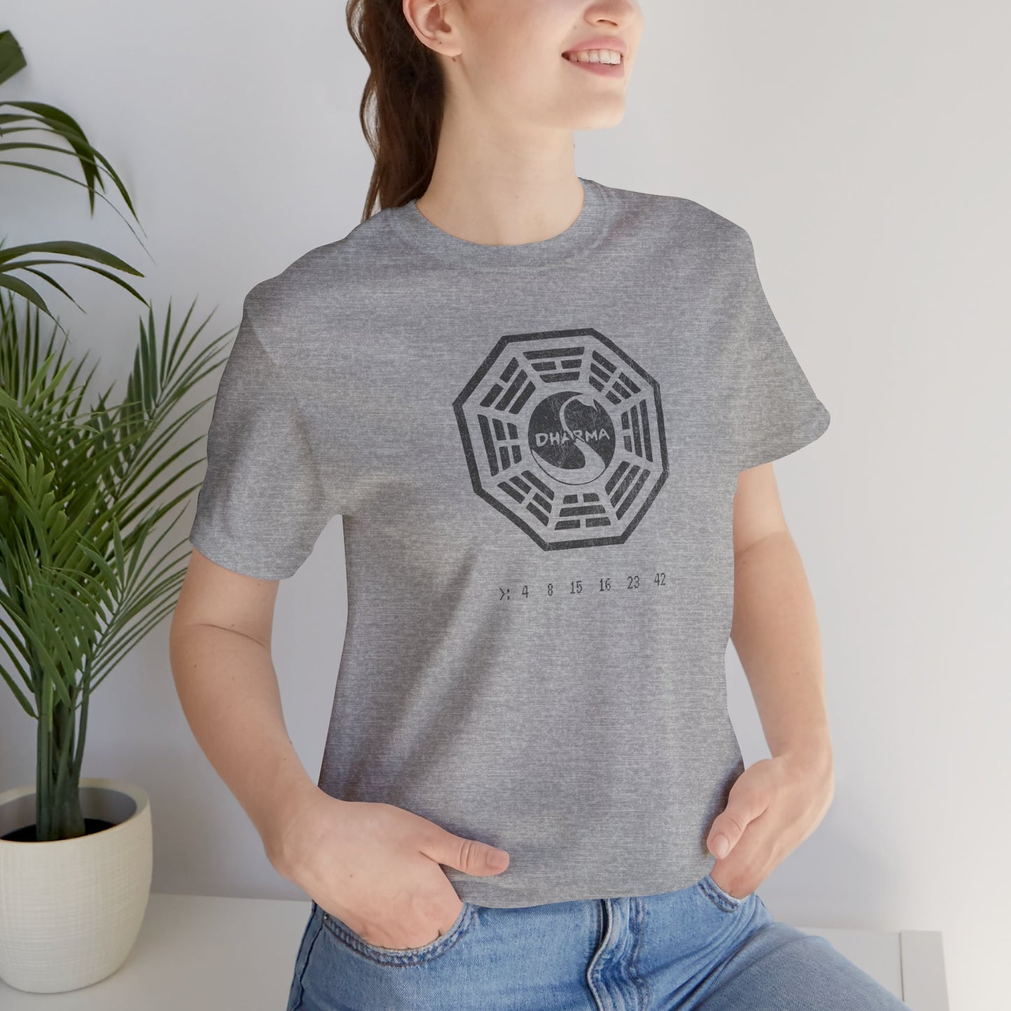 Female model wearing Athletic heather gray short-sleeve t-shirt featuring the Dharma Initiative swan station logo graphic from the TV show LOST in a vintage distressed style.
