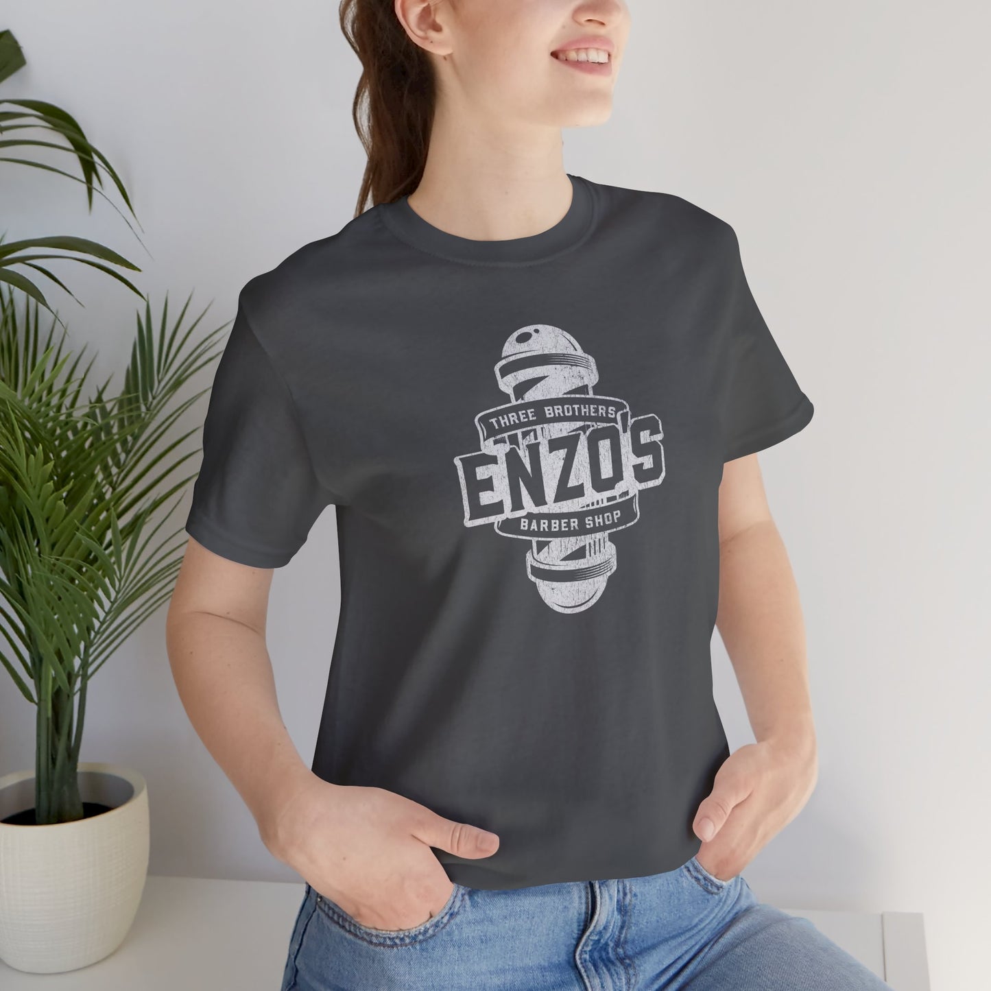 Woman wearing an asphalt gray t-shirt with the Enzo's Barber Shop logo graphic inspired by the TV show Seinfeld in a vintage distressed style.