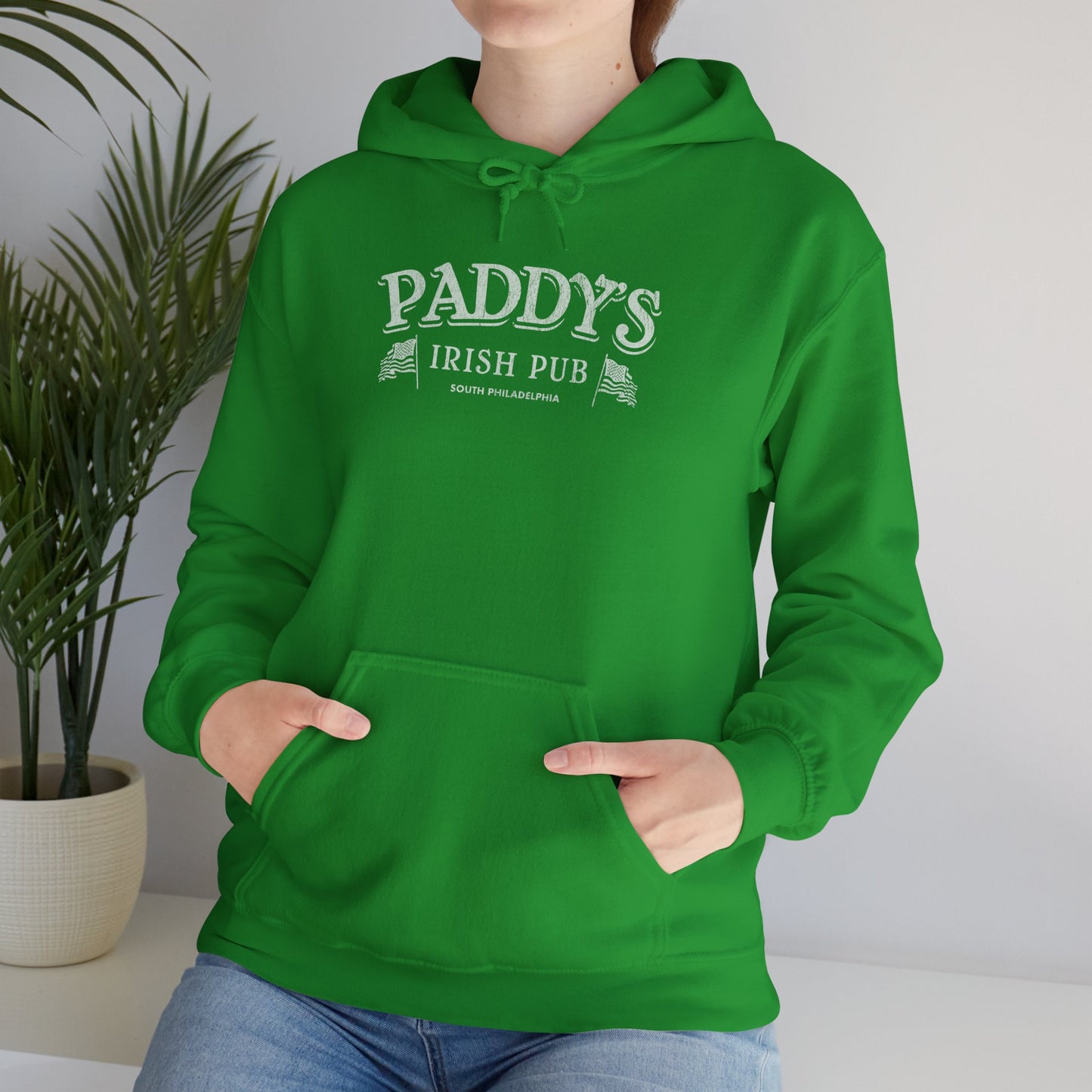 Female model wearing an Irish green colored soft unisex Hoodie Heavy Blend Hooded Sweatshirt featuring the Paddy's Pub logo graphic from the TV Show It's Always Sunny in Philadelphia, in a vintage distressed style, sold by ScriptedBrand.