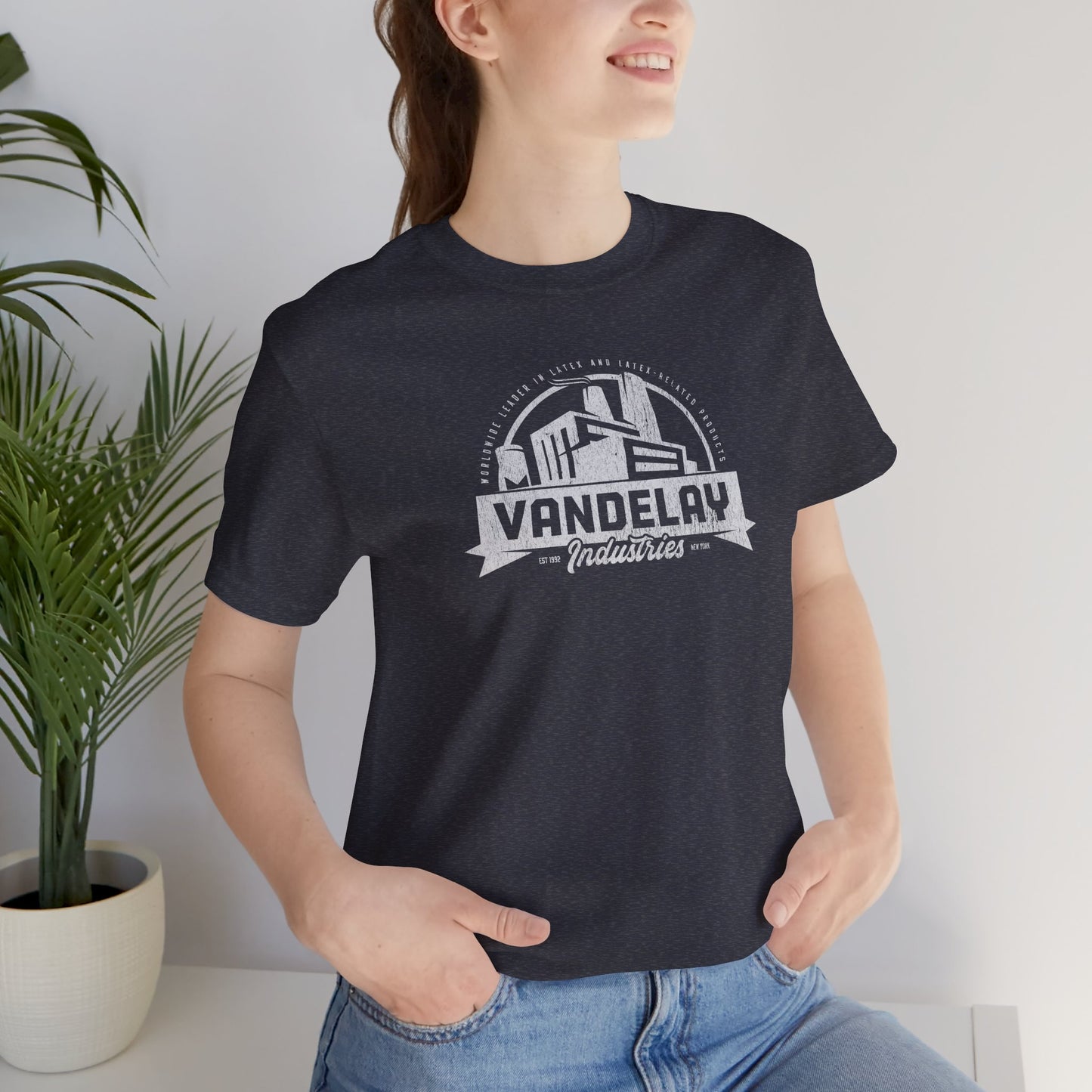 Female model wearing a Heather Navy Soft Bella+Canvas 3001 short-sleeve t-shirt tee featuring a Vandelay Industries logo graphic, uniquely designed by ScriptedBrand in a vintage distressed style. The fictional company is part of the George Costanza storyline in the TV show Seinfeld.
