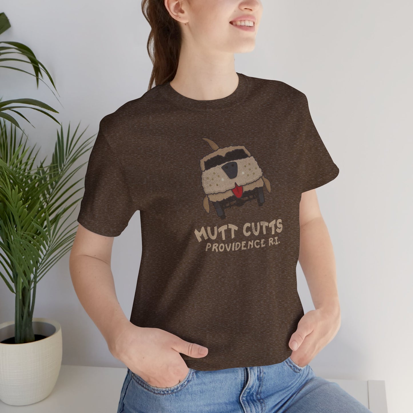 Female model wearing a heather brown colored Soft unisex Bella+Canvas 3001 short-sleeve t-shirt featuring a Mutt Cutts logo graphic inspired by the movie Dumb and Dumber, illustrated by ScriptedBrand in a vintage distressed style.