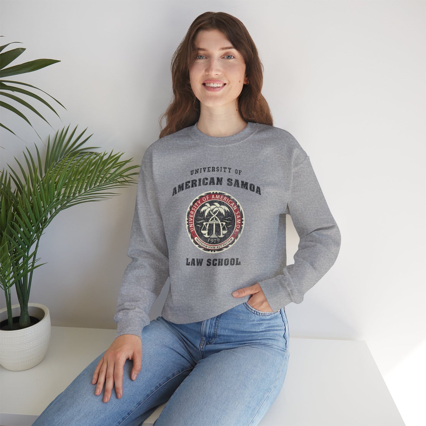 Woman wearing a gray sweatshirt with 'University of American Samoa Law School' text and logo, sitting indoors.