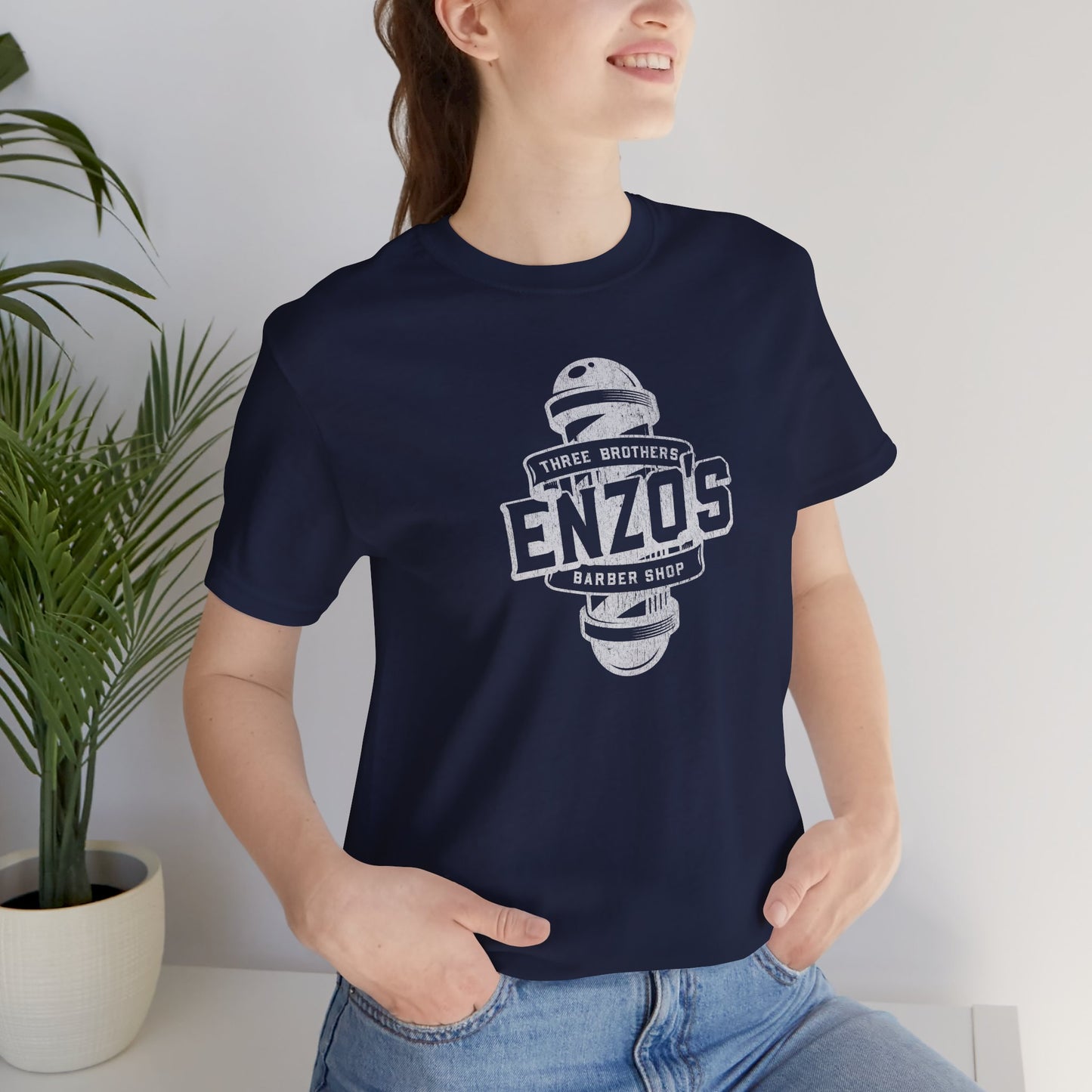 Woman wearing a navy blue t-shirt with the Enzo's Barber Shop logo graphic inspired by the TV show Seinfeld in a vintage distressed style.