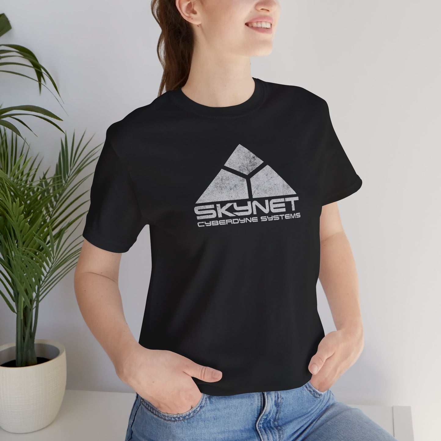 Person wearing a black t-shirt featuring the fictional logo Skynet Cyberdyne Systems from the movie The Terminator in a vintage distressed style.