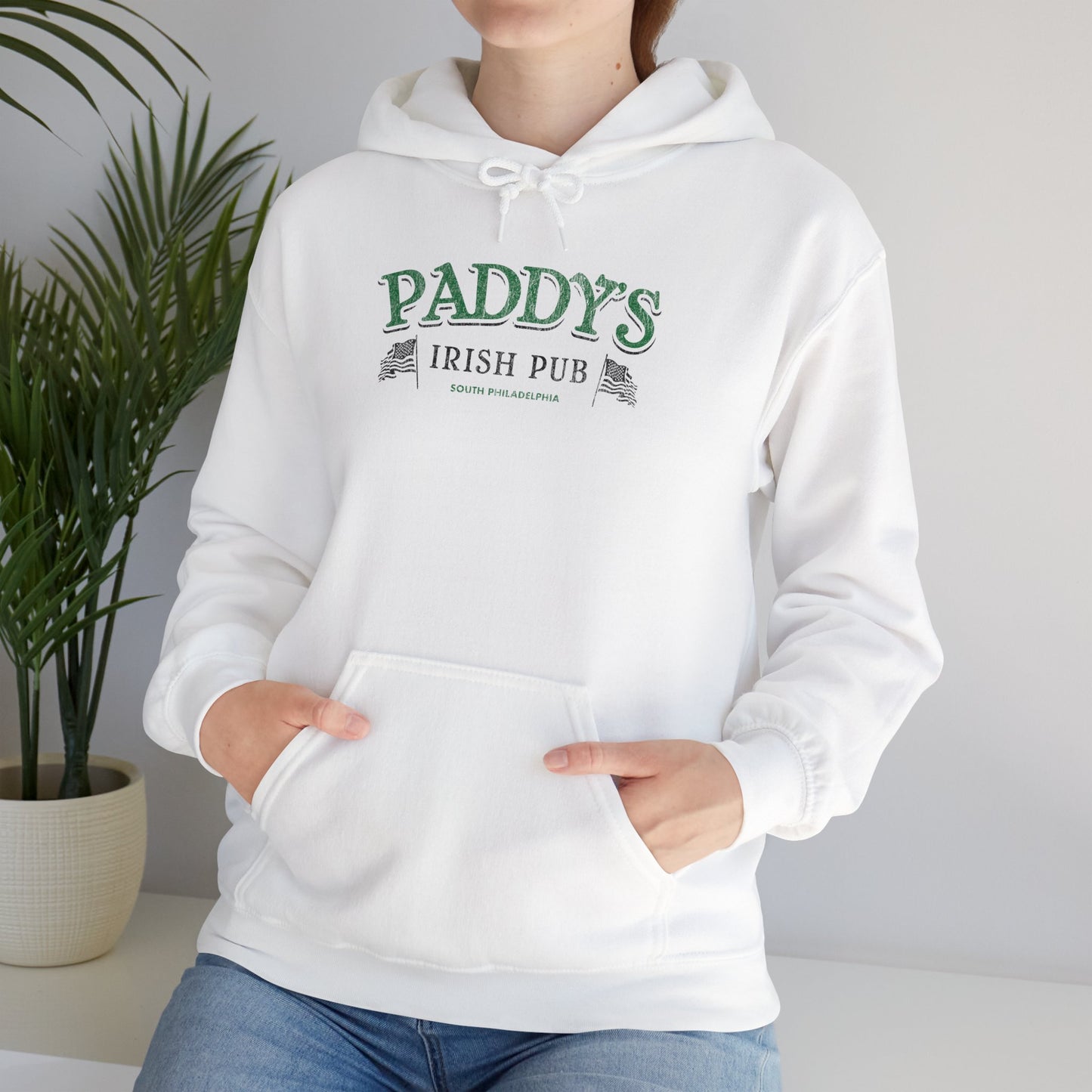 Female model wearing a white colored soft unisex Hoodie Heavy Blend Hooded Sweatshirt featuring the green Paddy's Pub logo graphic from the TV Show It's Always Sunny in Philadelphia, in a vintage distressed style, sold by ScriptedBrand.
