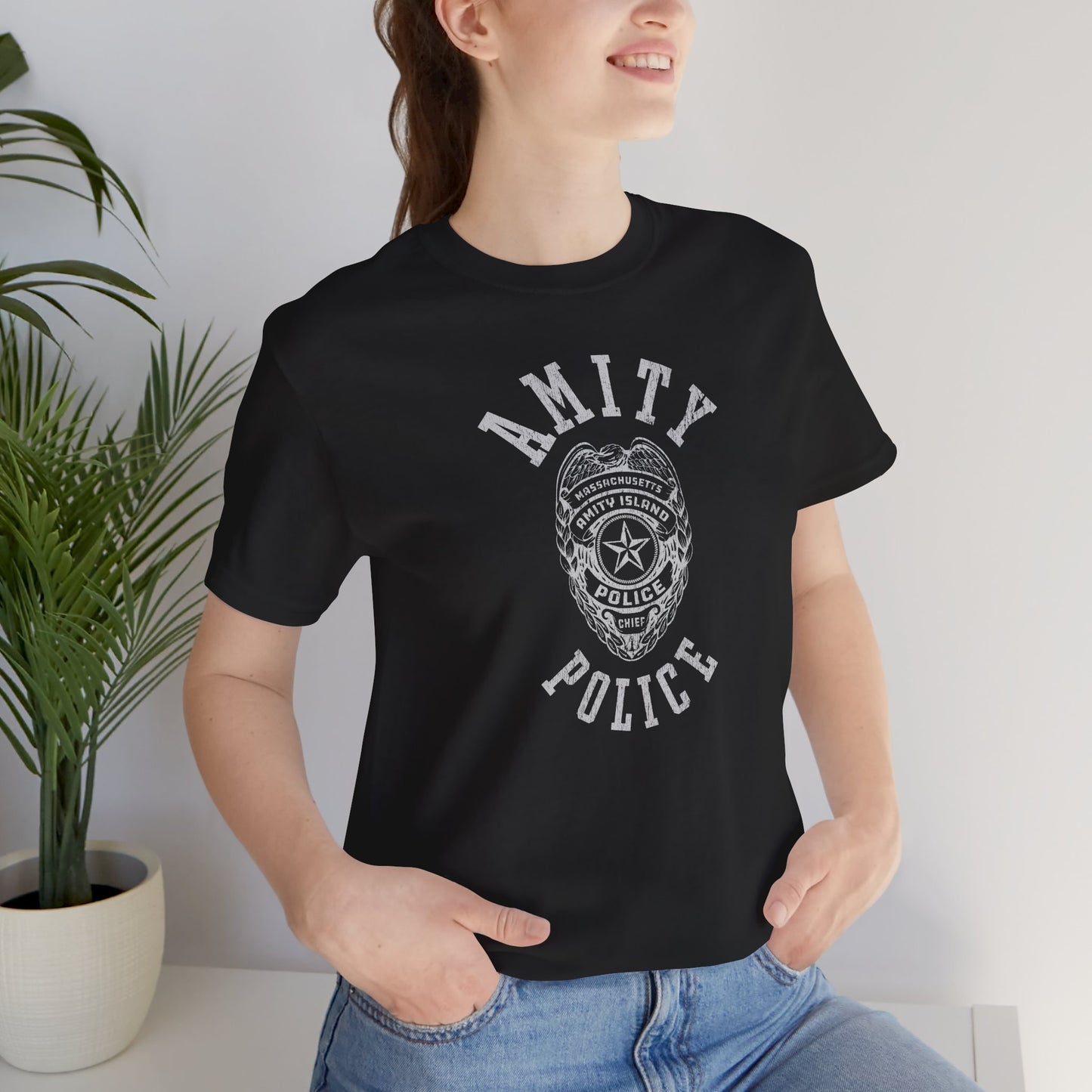 Female model wearing a black colored Soft unisex Bella+Canvas 3001 short-sleeve t-shirt featuring an Amity Island Police logo graphic, designed by ScriptedBrand, and inspired by the movie Jaws in a vintage distressed style.