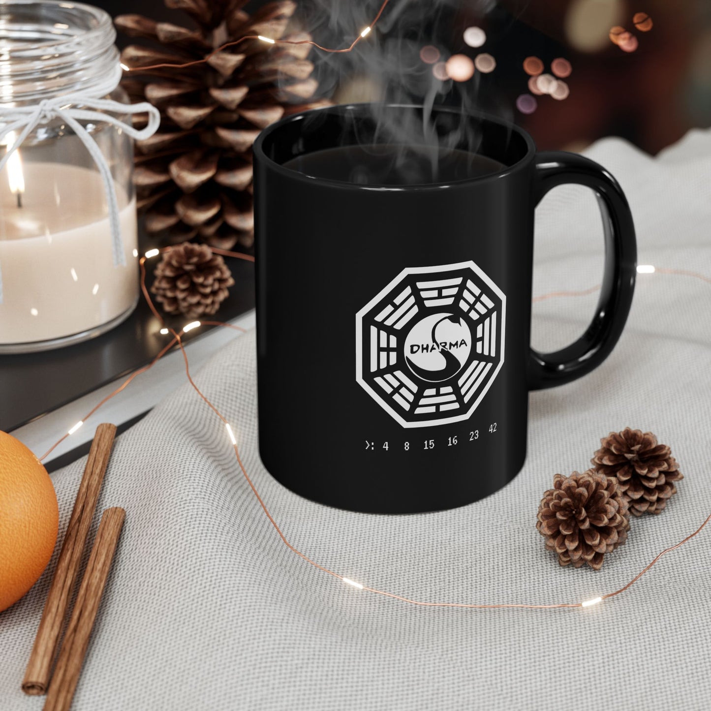 Angled view of a Black Ceramic Mug on a table featuring the Dharma Initiative swan station logo from the TV show LOST, including the Hatch numbers 4 8 15 16 23 42. Graphic is printed white on both sides.