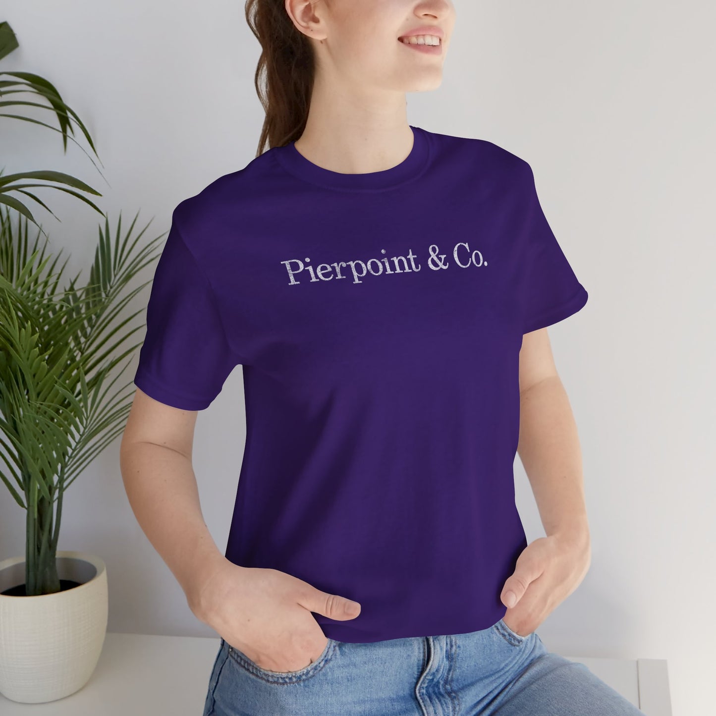 Female model wearing a purple soft short-sleeve Bella+Canvas 3001 t-shirt featuring the fictional logo Pierpoint & Co from the HBO TV show Industry in a vintage distressed style, sold by ScriptedBrand.