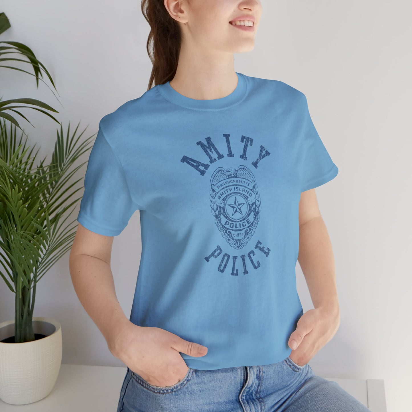 Female model wearing an ocean blue colored Soft unisex Bella+Canvas 3001 short-sleeve t-shirt featuring an Amity Island Police logo graphic, designed by ScriptedBrand, and inspired by the movie Jaws in a vintage distressed style.