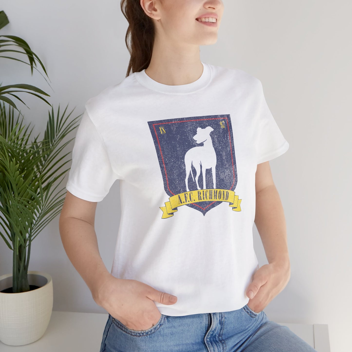 Female model wearing a white soft Bella+Canvas 3001 short-sleeve t-shirt featuring the logo graphic of the fictional English soccer team AFC Richmond inspired by the TV show Ted Lasso in a vintage distressed style, sold by ScriptedBrand.