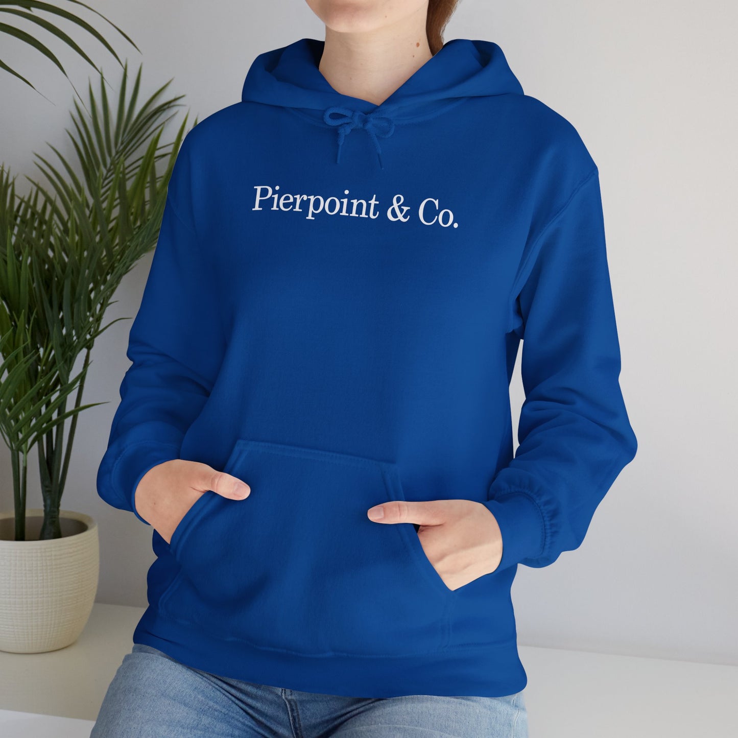 Female model wearing a royal blue soft Unisex Hoodie Heavy Blend Hooded Sweatshirt featuring the Pierpoint & Co logo worn by the character Eric Tao in the TV show Industry.