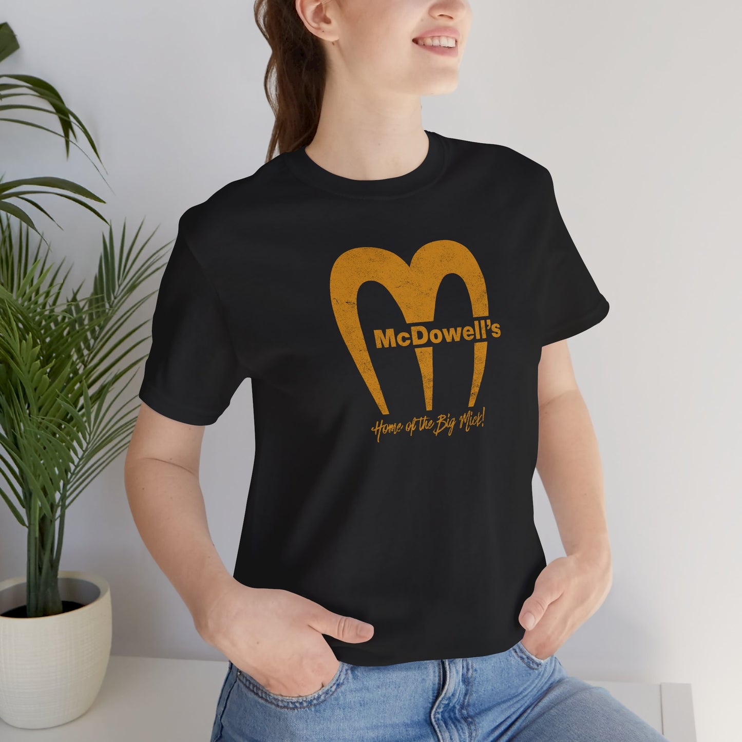Woman wearing a black t-shirt featuring the McDowells logo from the movie Coming to America in a vintage distressed style.