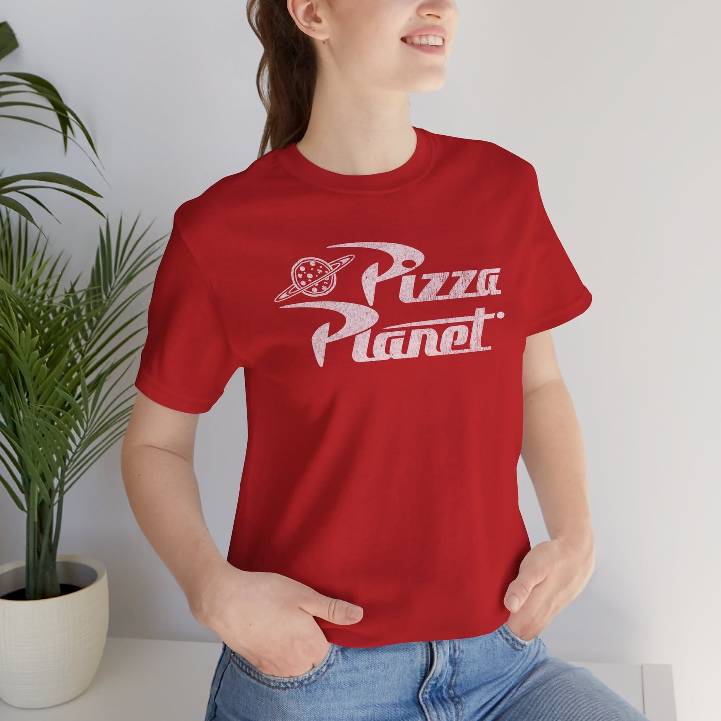 Woman wearing red t-shirt with distressed white Pizza Planet logo inspired by the Toy Story movies.
