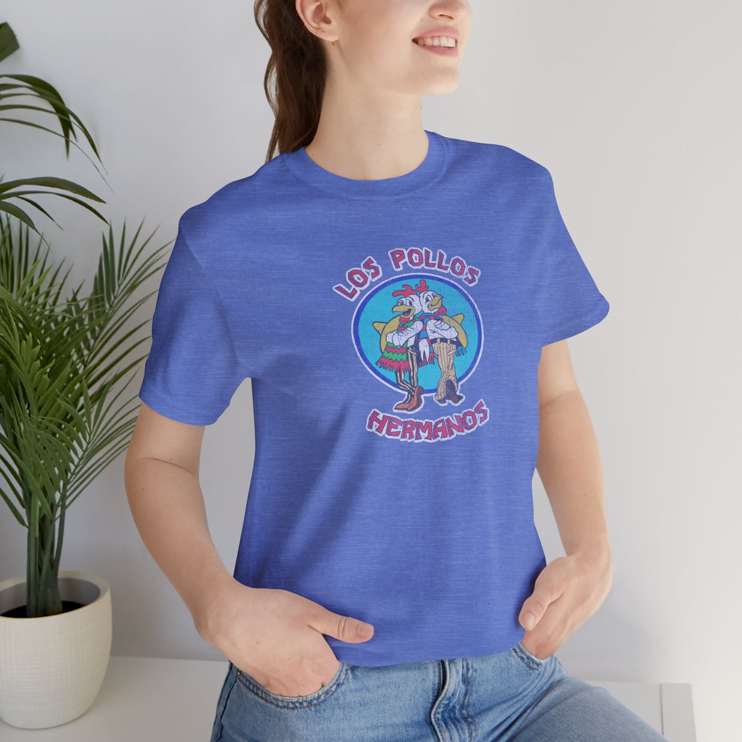 Female model wearing a Columbia Heather Blue Soft short-sleeve Bella+Canvas 3001 t-shirt featuring the Los Pollos Hermanos logo graphic from the TV show Breaking Bad in a vintage distressed style.