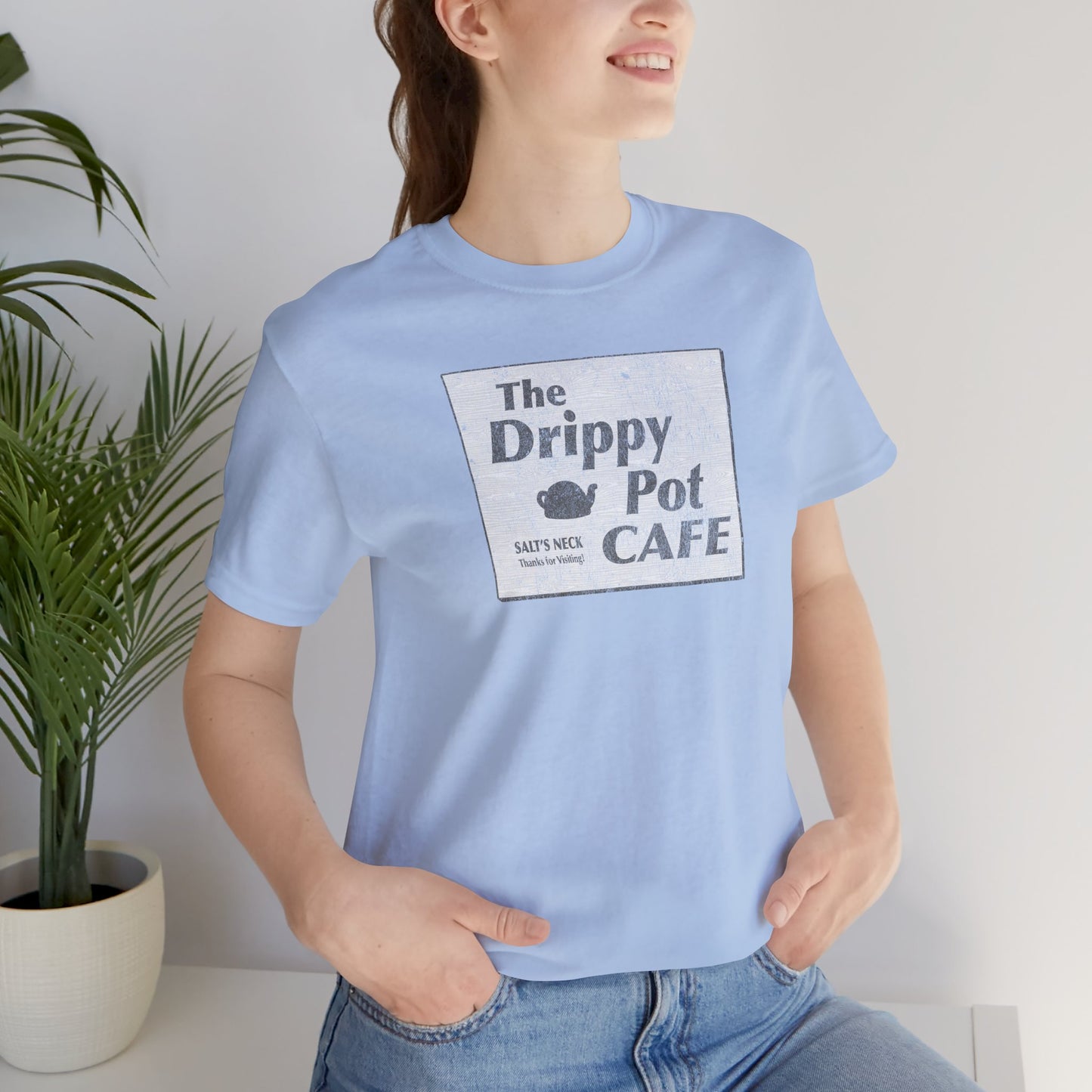Female wearing Bella+Canvas baby blue short-sleeve t-shirt featuring vintage Drippy Pot Café logo from Severance TV show, unisex fit