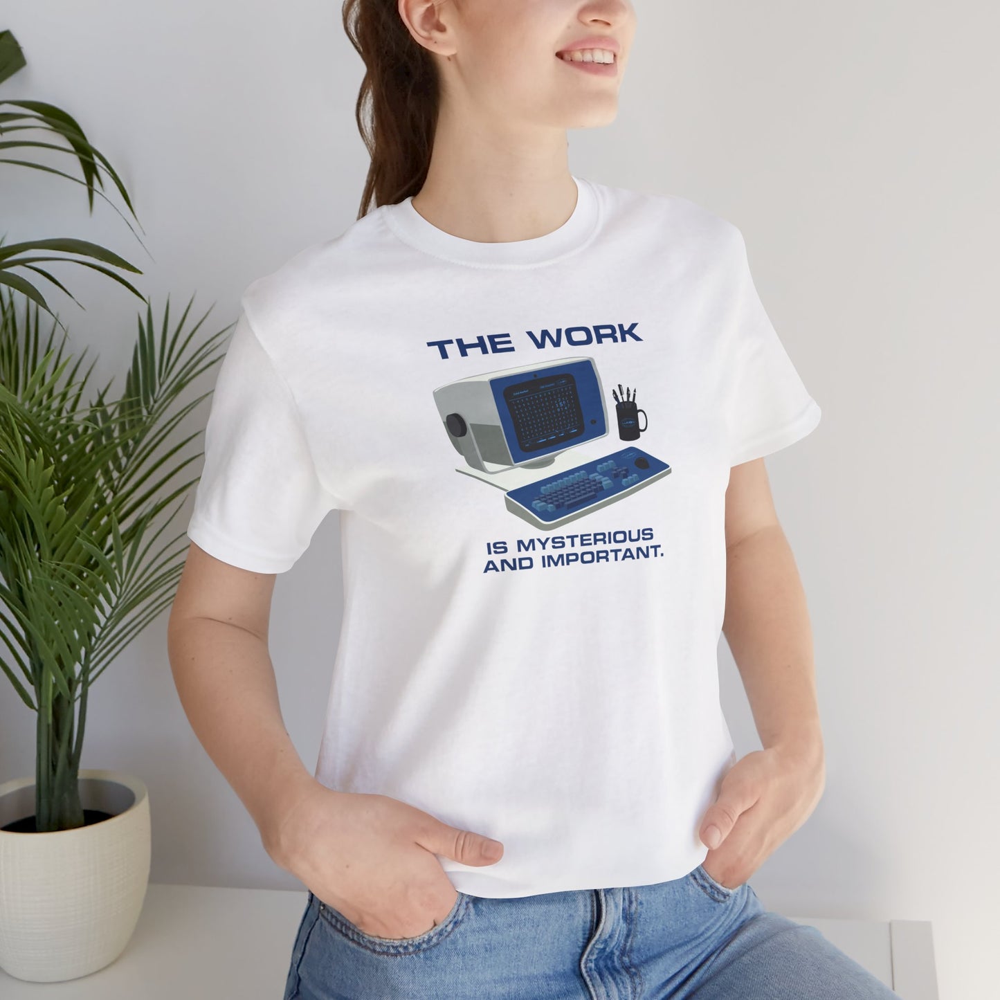 Female model wearing a white Soft Bella+Canvas shirtsleeve t-shirt featuring the retro computer workstation from the Apple TV show Severance, and includes the text The Work is Mysterious and Important. Graphic is designed and illustrated by ScriptedBrand.