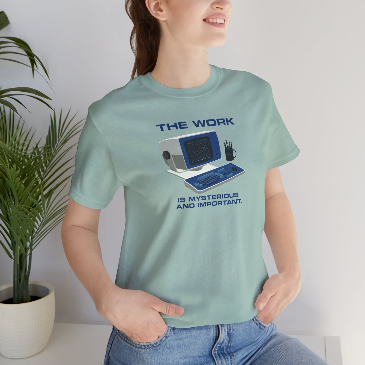 Female model wearing a dusty blue Soft Bella+Canvas shirtsleeve t-shirt featuring the retro computer workstation from the Apple TV show Severance, and includes the text The Work is Mysterious and Important. Graphic is designed and illustrated by ScriptedBrand.