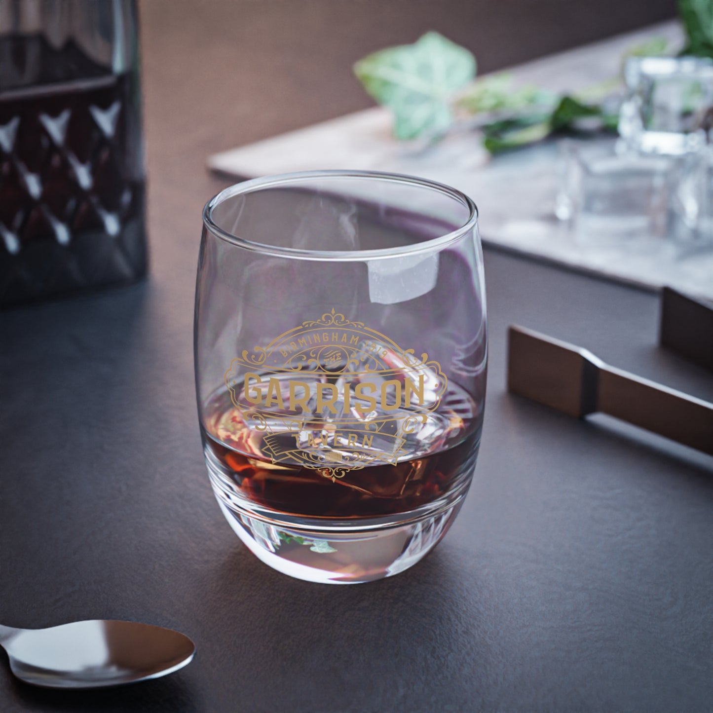 Mockup of a 6 ounce Whiskey Glass featuring the Garrison Tavern Bar Logo Graphic inspired by the TV show and movie Peaky Blinders printed on one side, sold by ScriptedBrand, and shown on a table.