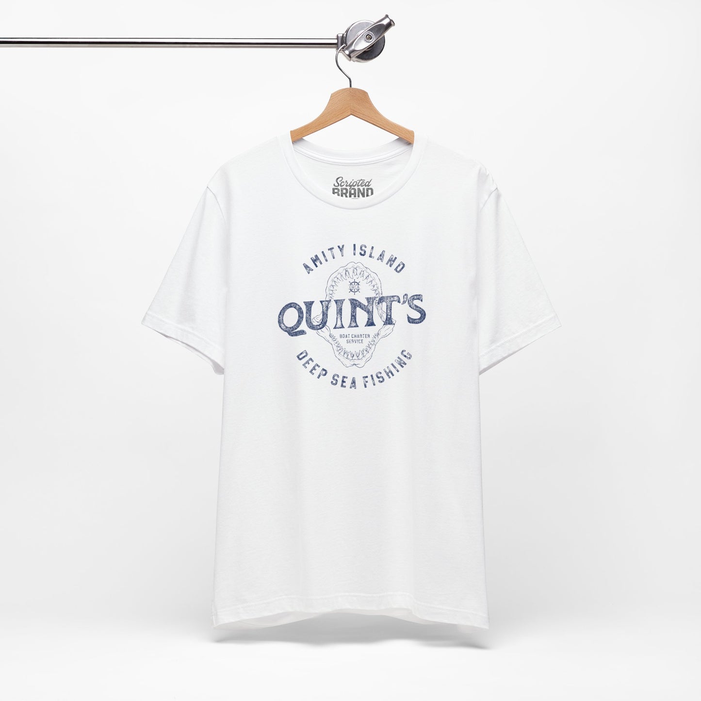 White colored Soft short-sleeve t-shirt on a hanger featuring the Quint's Deep Sea Fishing Boat Charters logo graphic inspired by the movie Jaws in a vintage distressed ink-stamped worn-in style.